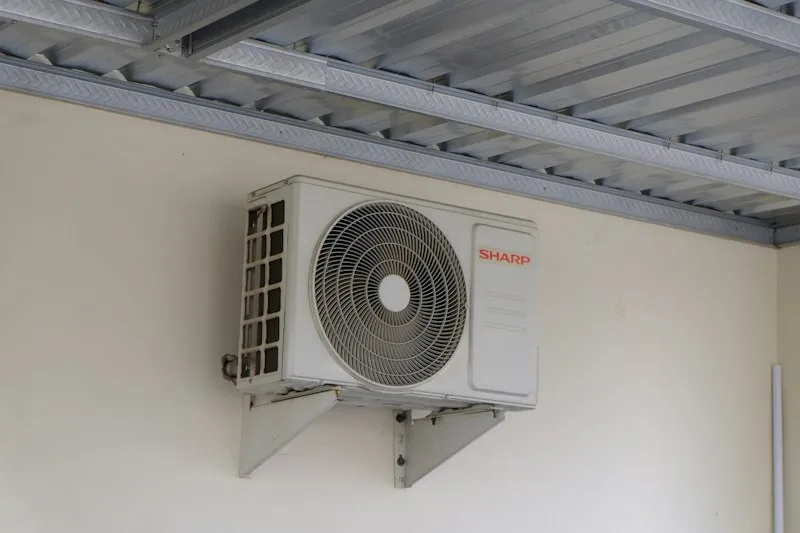 Newly installed aircon outdoor unit on a wall bracket under a roof eave